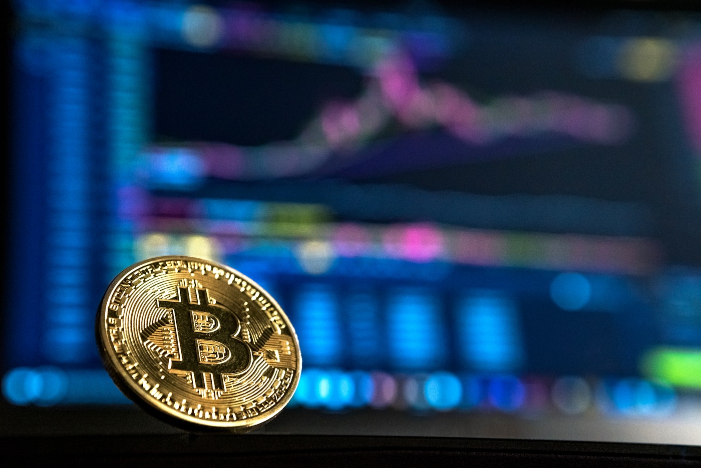A Bitcoin coin in front of a cryptocurrency trading screen