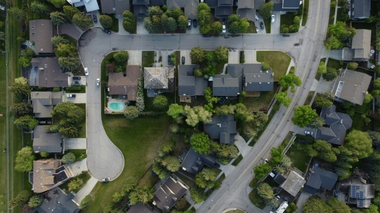 Overhead view of a suburban neighborhood of single-family homes around a cul-de-sac, with tree-lined yards and a backyard pool
