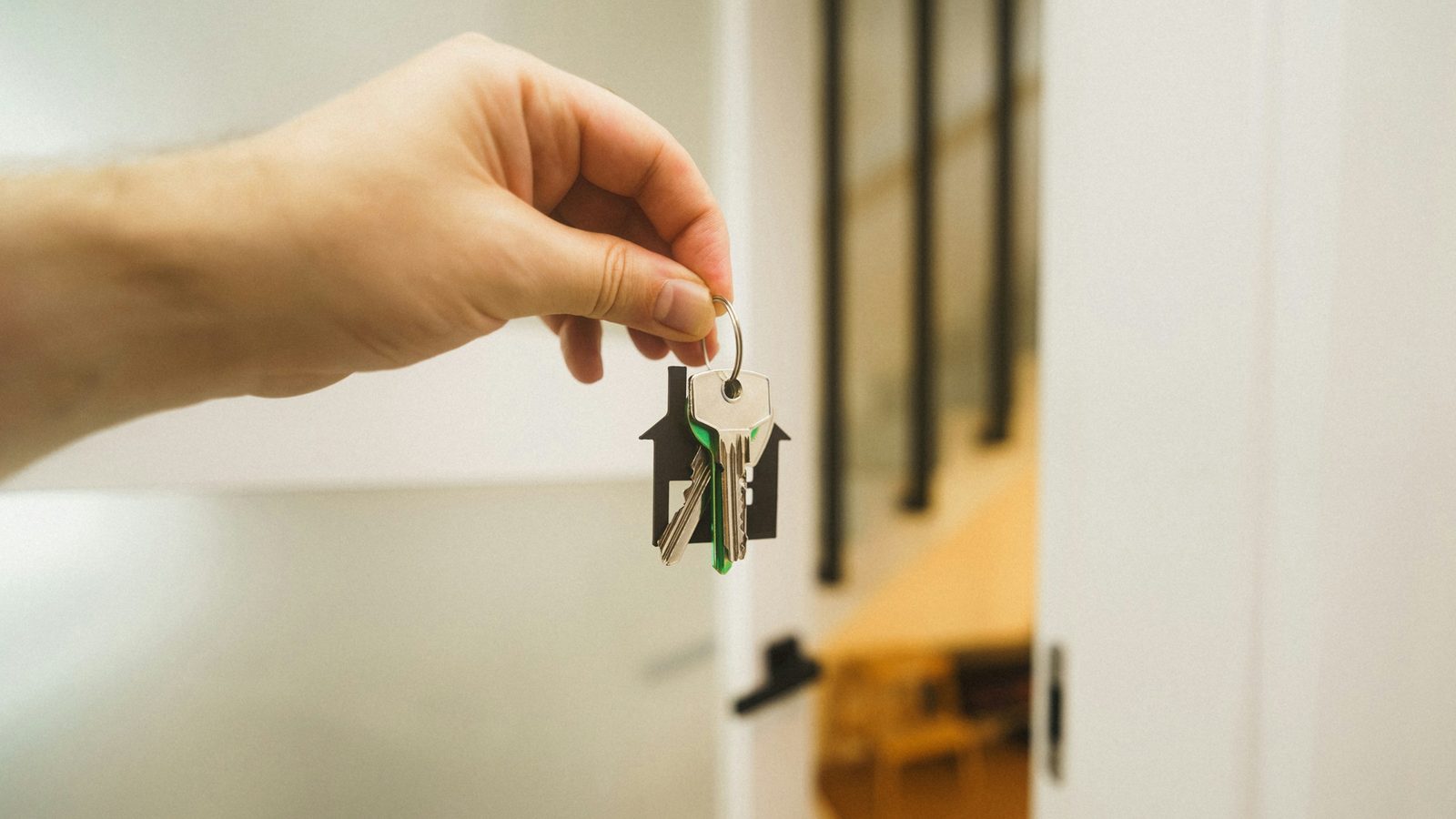 Hand holding house keys on a house-shaped key ring at an open front door, representing a rental property bought through a self-directed IRA