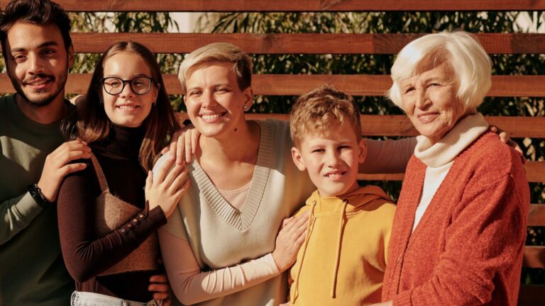 Three generations of a family smiling together outdoors, from a grandmother to her grandchildren