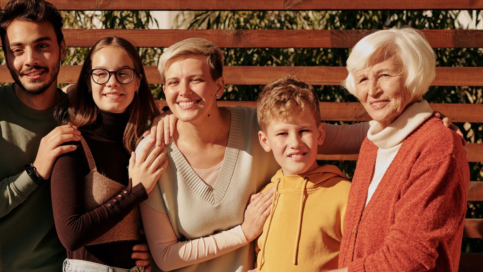 Three generations of a family smiling together outdoors, from a grandmother to her grandchildren