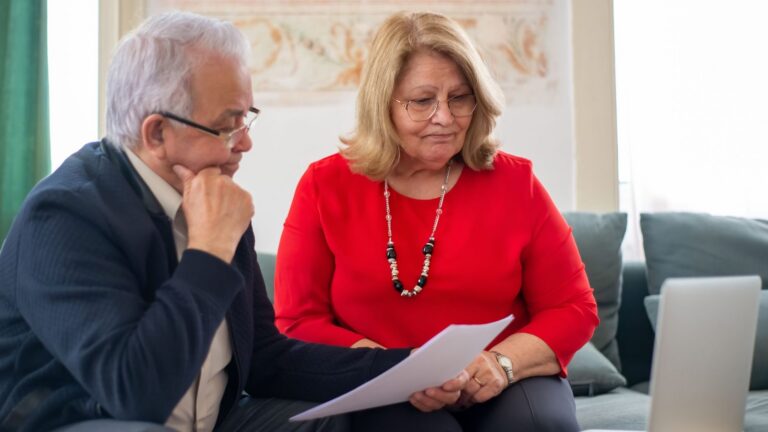 Retired couple reviewing self-directed Roth IRA paperwork together on a sofa in a bright sitting room