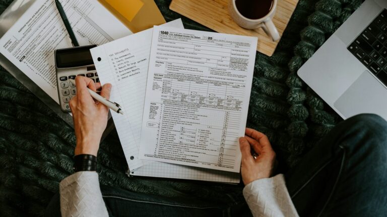 Tax forms, a calculator and a pen on a desk while someone works through tax calculations